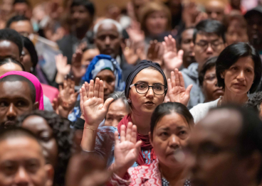 A women with her right hand raise and taking the Oath of Citizenship.