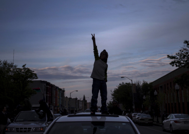 A boy reaches out to display a peace sign while celebrating from the roof of car in Baltimore.